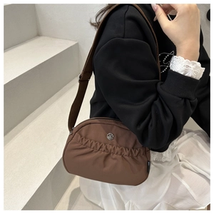 Detailed close-up of brown nylon crossbody bag with metal M logo and wide strap on model