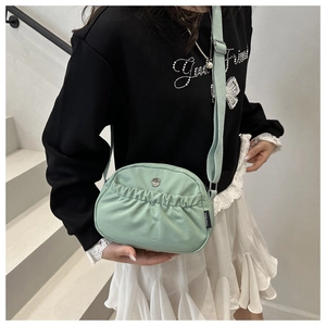 Detail view of mint green nylon pleated bag with round metal logo and adjustable strap