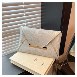 Detail of white snakeskin texture clutch with gold metal trim on a minimalist book