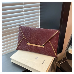 Macro detail of wine red snakeskin texture envelope clutch with gold metal trim