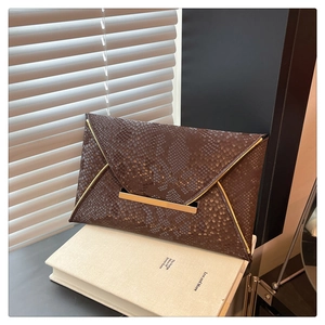 Détail de la pochette enveloppe marron foncé motif serpent avec garniture en métal doré