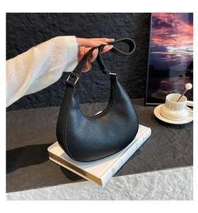Detail of black lychee grain leather crescent bag with gold metal buckle and strap