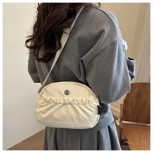 Detail of off-white canvas crossbody bag with pleated front and metal buckle on strap