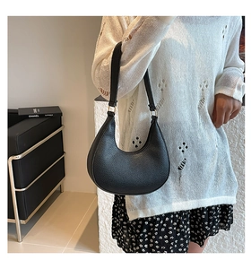 Detail of black pebbled leather crescent bag with gold-tone buckle on model shoulder