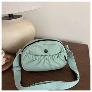 Detailed macro view of mint green nylon crossbody bag with pleated front and metal logo