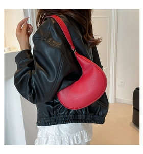 Close-up of red lychee textured crescent bag worn with a black leather jacket