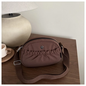 Close-up of a brown crossbody bag with a ruched front pocket and a round metal M logo