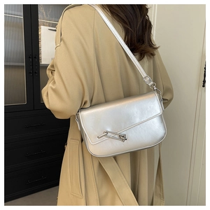 Detail of silver saddle bag with metallic mirror finish and adjustable strap on a model