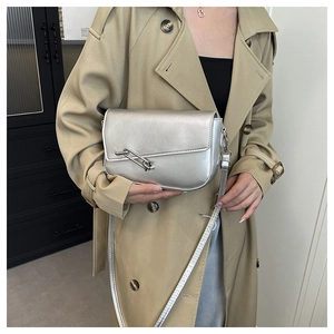 Detail of silver flap shoulder bag with unique metal safety pin buckle on khaki trench coat