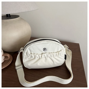 Close-up of cream crossbody bag featuring a round metal M logo and black zipper detail