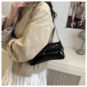 Vue latérale du sac à bandoulière en cuir verni noir porté avec une tenue chic