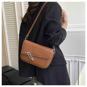 Brown leather shoulder bag with silver buckle worn by a model in minimalist interior