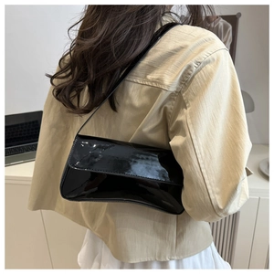 Side view of a glossy black patent leather underarm bag worn with a casual outfit