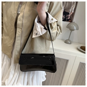 Détail d'un sac baguette en cuir verni noir porté à l'épaule pour femme