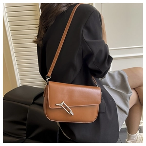 Detail of a brown leather saddle bag with a large silver pin buckle worn by a model