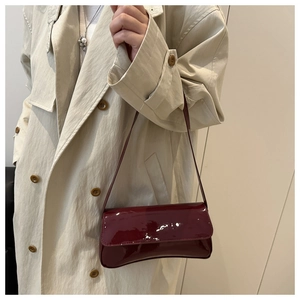 Détail d'un sac baguette en cuir verni rouge vin porté avec un trench-coat élégant
