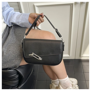 Detail of black matte leather saddle bag featuring a large silver safety pin buckle