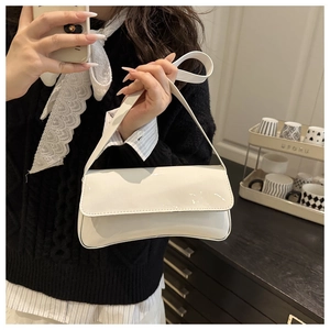 Detail shot of a white patent leather baguette shoulder bag shown on a female model