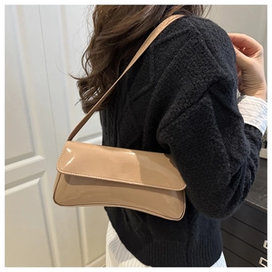 Détail du sac baguette en cuir verni beige brillant porté sur un pull en maille noire