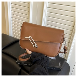 Detail of a brown leather shoulder bag featuring a unique silver metal pin-shaped lock