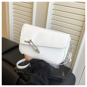 Detailed view of white leather shoulder bag featuring a unique oversized silver safety pin buckle