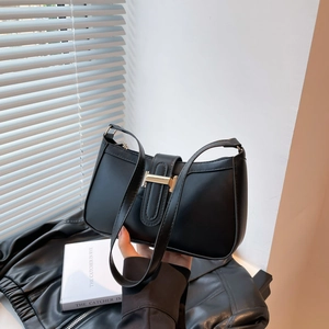 Klassische schwarze Leder-Halbmondtasche mit goldener H-Schnalle auf Buch und Lederjacke