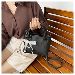 Detail of black lychee grain handbag with pearl bow lace pendant on a wooden bench