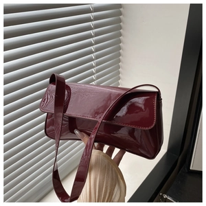 Détail de la texture en cuir verni brillant et du rabat du sac à bandoulière rouge foncé