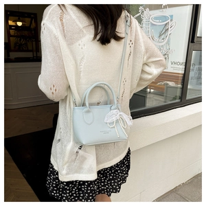 Detail of light blue leather bucket bag with lace bow and pearl charm ornament