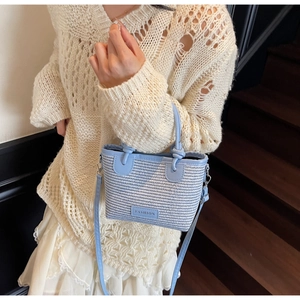 Close-up of blue and white woven straw bag featuring a fashion patch and leather handles