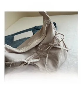 Close-up of beige half-moon nylon bag with pleated texture and decorative bow detail