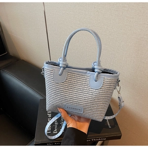 Close-up of light blue and white woven straw handbag with PU leather knot handle and straps