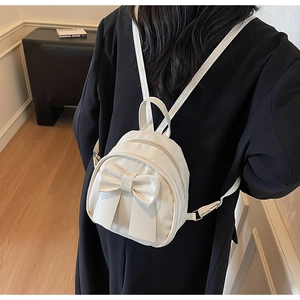Detailed view of a mini beige backpack with large bow detail worn on model's back