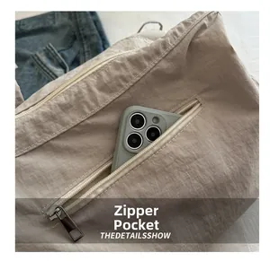 Detail of a casual pleated tote bag featuring a functional exterior zipper pocket for phones