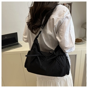 Gros plan du sac à bandoulière en toile noire avec nœuds et détails de sangle réglable