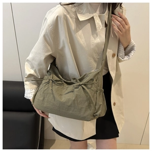 Detail of dark green pleated tote bag with bow drawstring design on adjustable strap