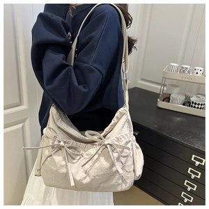 Detail of off-white pleated crossbody bag with decorative bows and side drawstring pockets