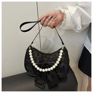 Détail d'un sac hobo en dentelle noire avec nœud en satin et anse en perles élégante