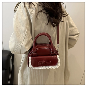 Red retro Boston bag with lace trim and bow detail styled on a beige trench coat
