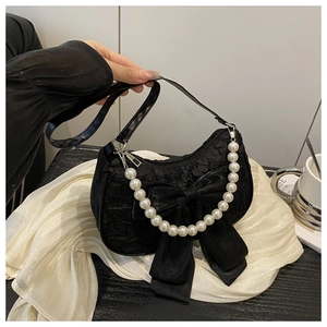 Détail du sac texturé noir avec grand nœud en satin et chaîne de perles décorative