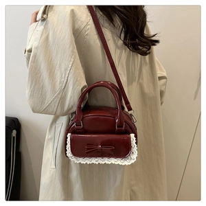 Sac rouge foncé verni avec dentelle et nœud porté sur un trench-coat beige