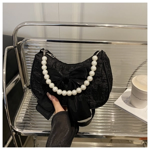 Détail du sac demi-lune noir avec tissu texturé, grand nœud et poignée en perles blanches
