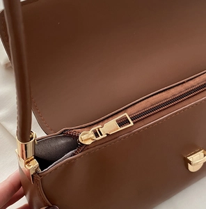 Detailed macro view of golden metal zipper and buckle on a brown leather shoulder bag