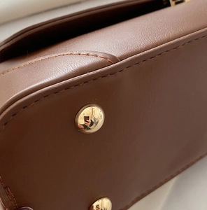Detail of gold metal feet on brown textured leather bag with premium stitching