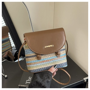 Detail of multi-color woven straw bag with brown leather flap and gold logo