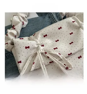 Detail of white pleated handbag featuring red polka dots and bow prints on denim background
