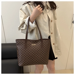 Sac cabas marron à motif monogramme et logo doré porté par un mannequin en manteau