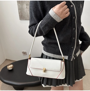 Close-up of white leather baguette bag with red trim and gold buckle detail