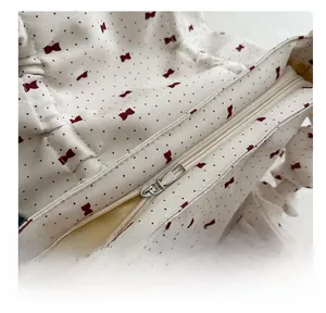 Close-up of smooth metal zipper and red bow print on the cream shoulder bag
