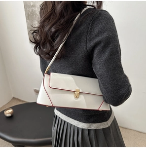 Close-up of a white baguette shoulder bag with red edge details and a gold cylindrical clasp